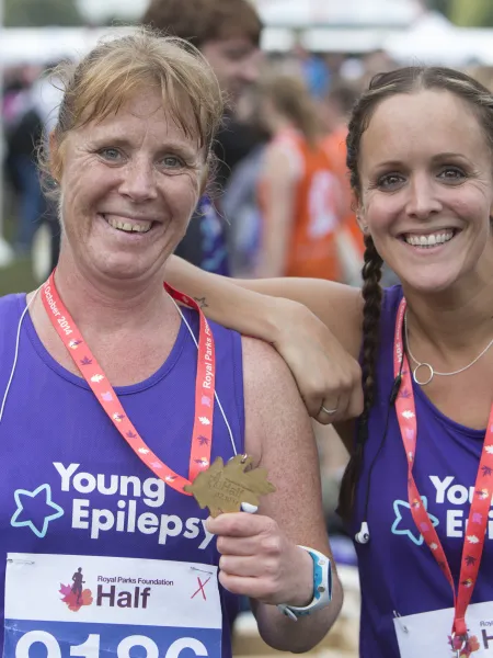 Two women in Young Epilepsy running vests, smiling at the camera proudly showing their medals.