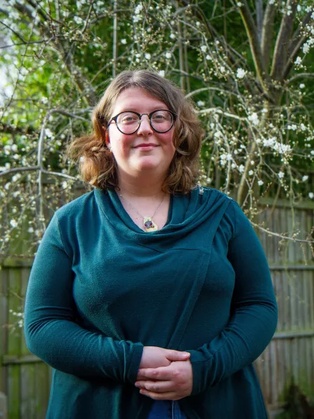 A young woman in a teal jumper and glasses smiles outside for a photo.