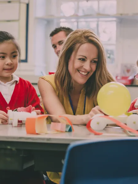 A teacher laughs alongside her students in a classroom.