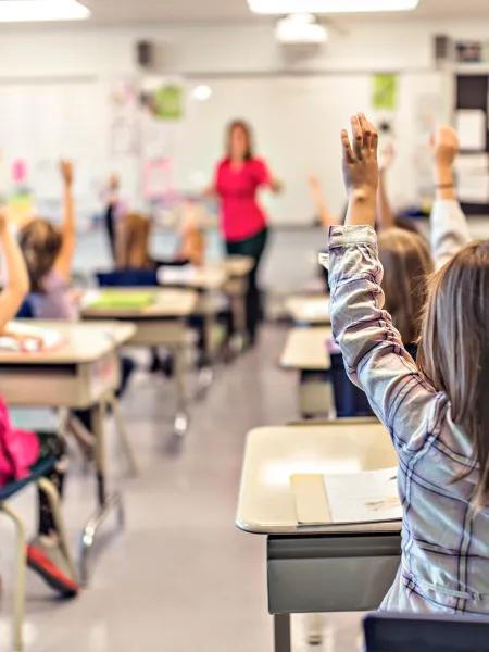 School children in a classroom with their hands up
