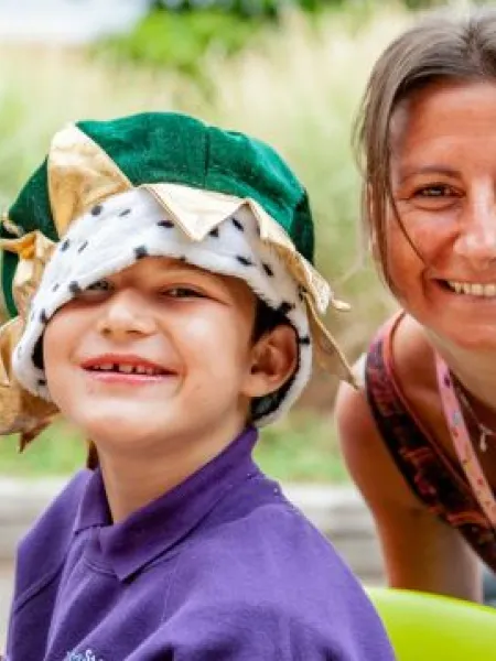 Young boy wearing a green velvet crown sat next to an adult woman. Both are smiling towards the viewer.