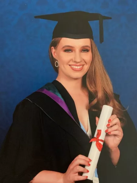 A young woman holds her degree and smiles in a graduation photo.