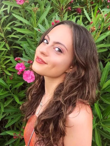 Olivia, a young woman, smiles in a selfie before a flowery bush.
