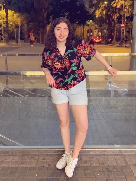 A young woman in a floral shirt smiles for a photo taken at night.