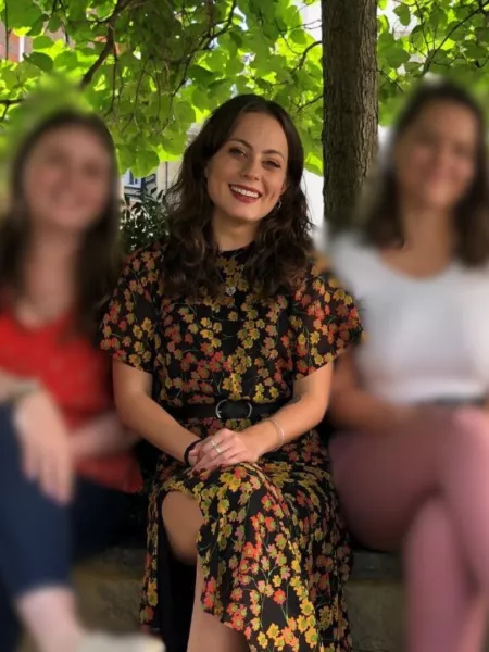 A smiling woman in a floral dress sits between two other women, whose faces are blurred.