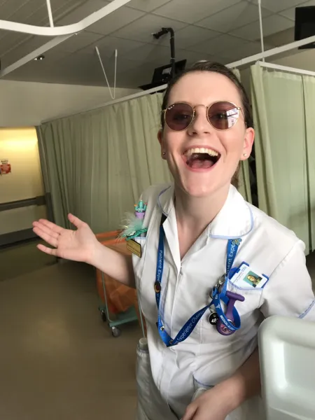 A nurse wearing sunglasses smiles widely to the camera while working on a ward.