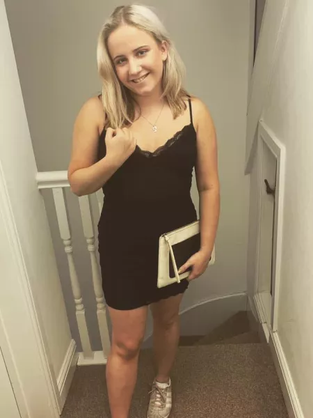 A girl in a black dress holds a notebook and smiles for a photo.