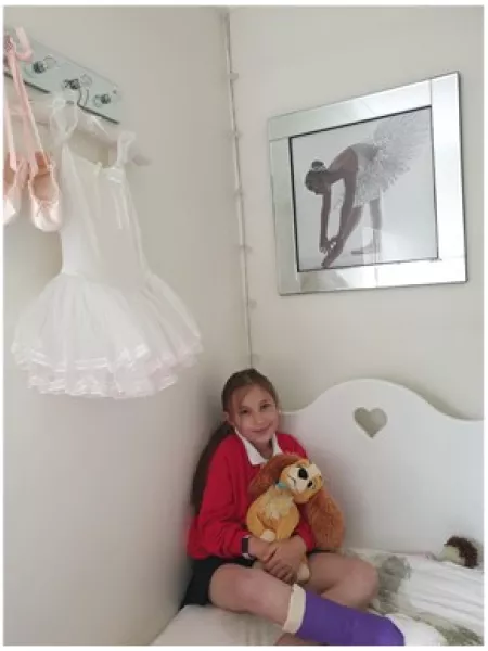 A girl in a leg cast holds a stuffed animal in bed.