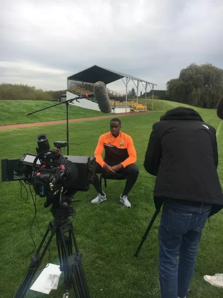 A young man sits before film cameras on a football pitch for a Christmas appeal.