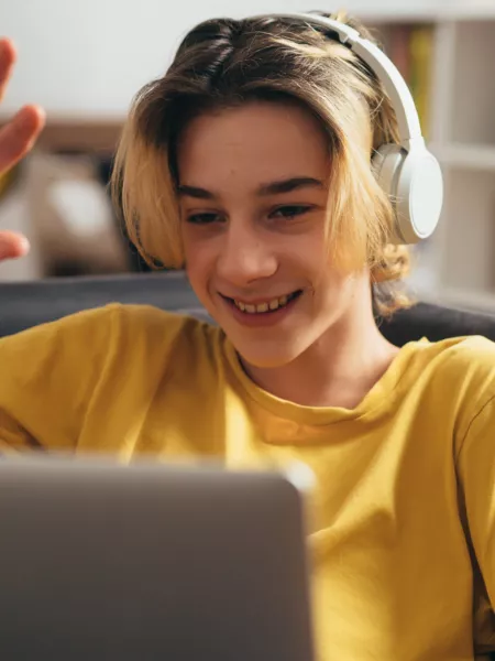 Young boy wearing headphones, waving and smiling on a video call