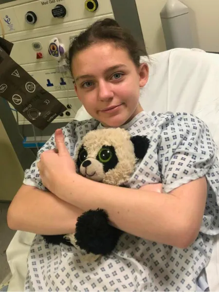 Young girl clutching soft toy on hospital bed.