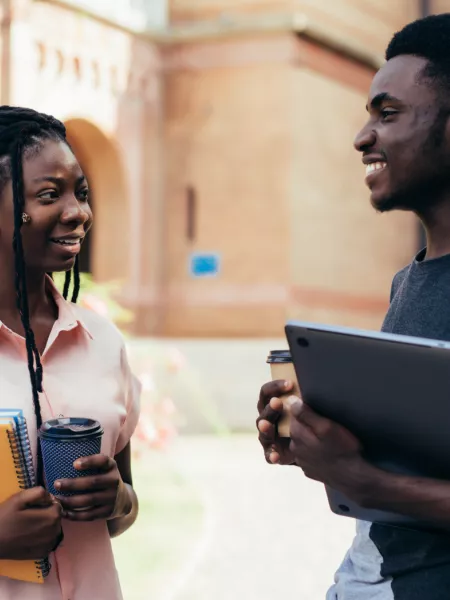 young male and female chat at a university campus with notebooks and coffee in hand.