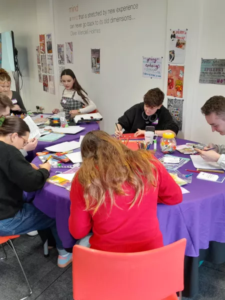 A group of young people from Young Epilepsy sit at a table putting together a pamphlet.