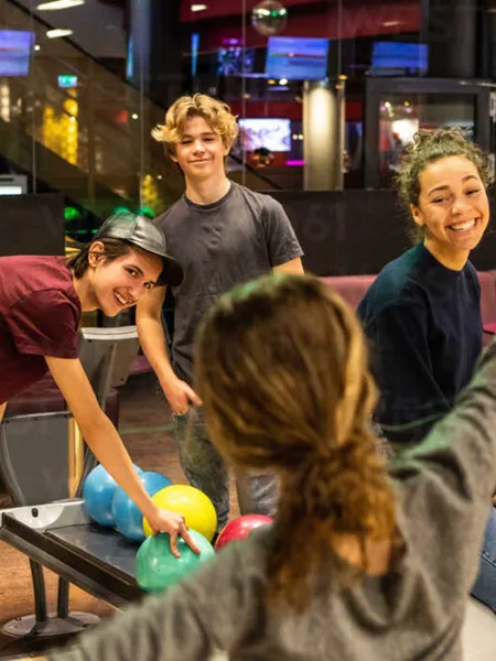 Four young people smile and laugh as they gather around a bowling alley.