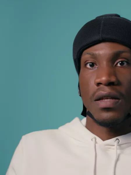 A young boy in a wheelchair with a protective helmet against a blue backdrop wearing a white t-shirt
