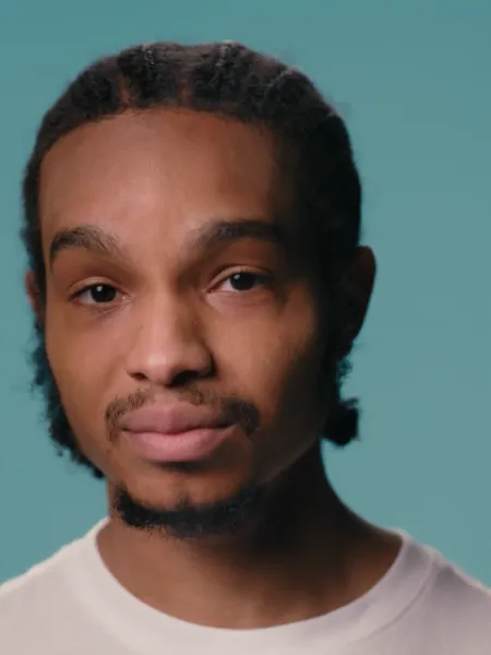 A young black boy stands against a blue backdrop wearing a white t-shirt