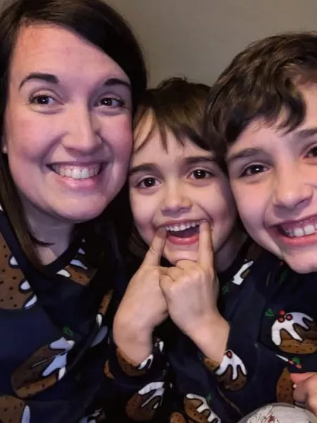 A woman and two boys smile widely in Christmas jumpers.