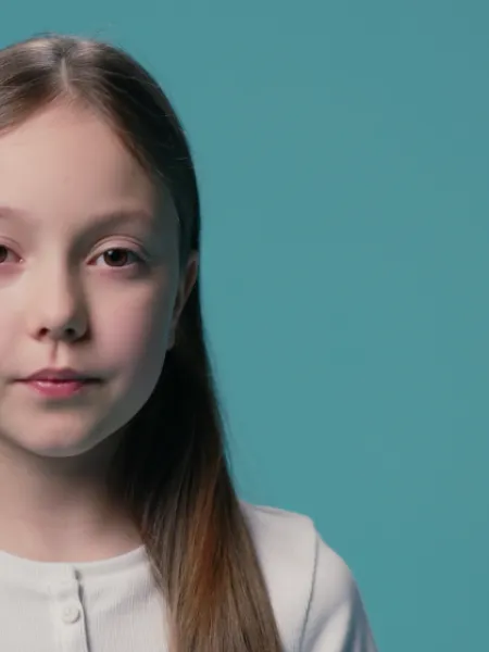 A young Caucasian girl stands against a blue backdrop wearing a white t-shirt