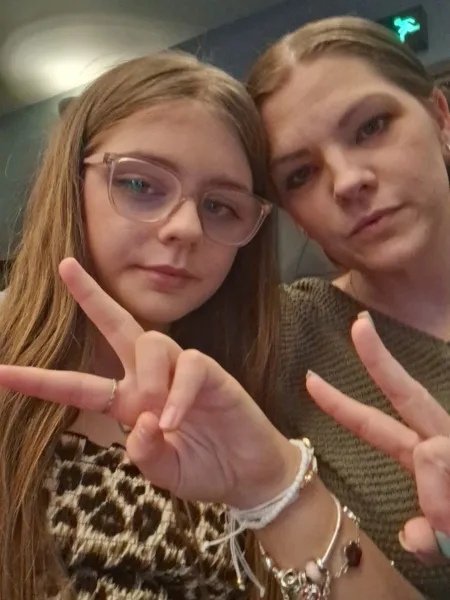 A mother and daughter pose with peace signs in a selfie.