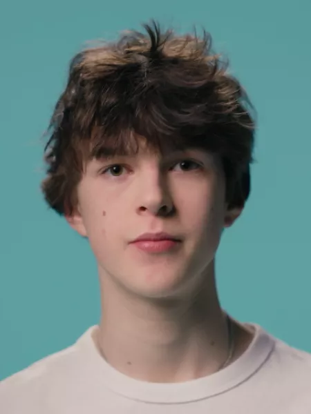 A young boy stands against a blue backdrop wearing a white t-shirt