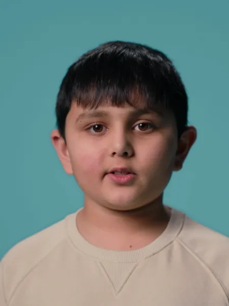 A young Asian boy stands against a blue backdrop wearing a white t-shirt
