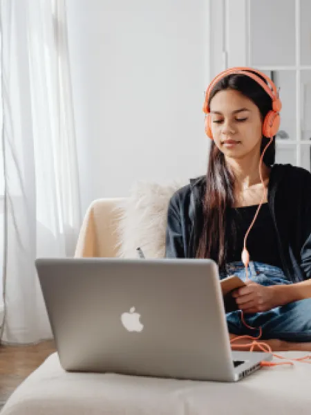 Teenage girl wearing headphones looking at laptop for an online video call.
