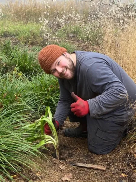 A young man smiles as he tends his garden.