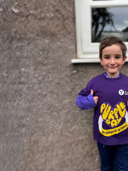 Young boy smiles with thumbs up wearing a 26 miles for 26 days for purple day t-shirt
