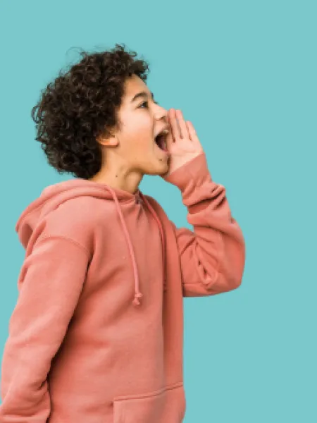 Young boy holding palm to face shouting to the distance against a blue backdrop.